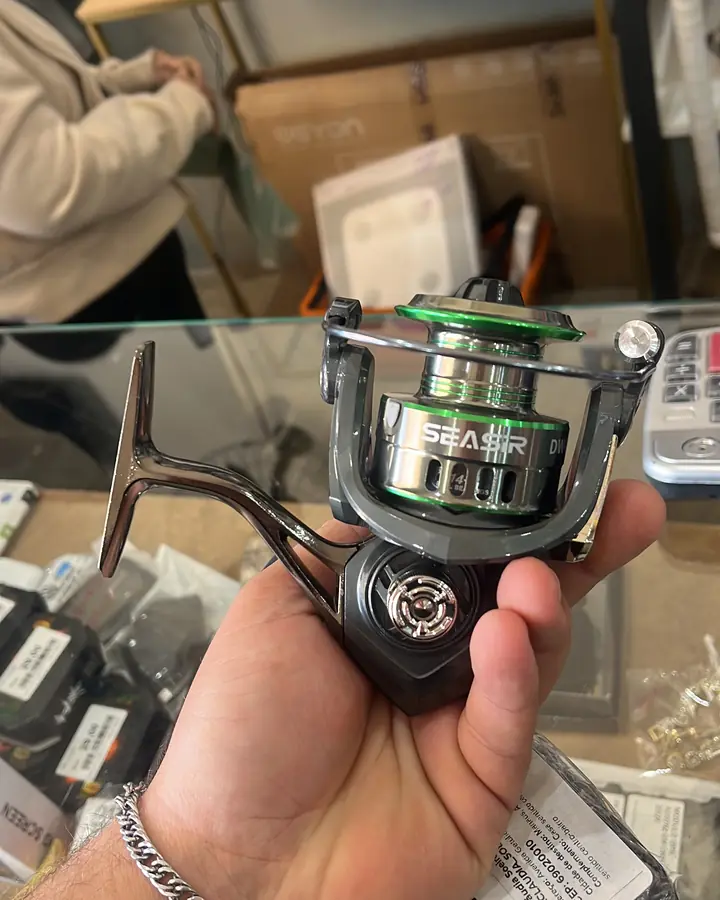 Molinete de pesca preto e verde segurado sobre o balcão de vidro