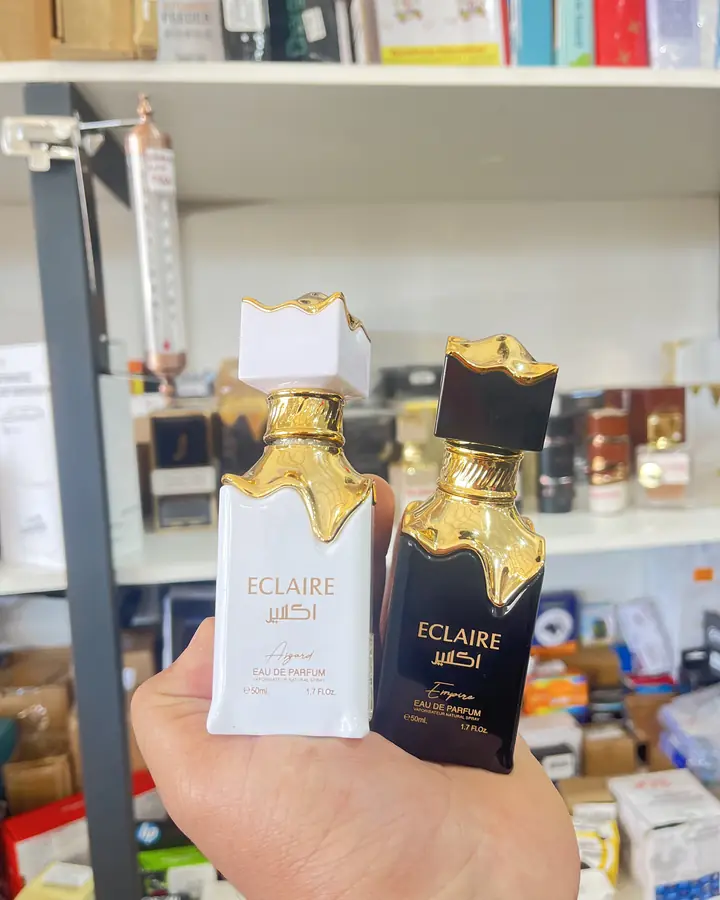 Dois frascos de perfume Eclaire, um branco e um preto, segurados na frente da prateleira de perfumaria